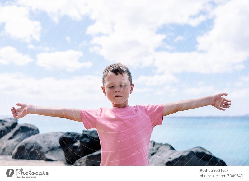 Entspannter Junge, der mit geschlossenen Augen am Meer steht meditieren MEER Stein Windstille Yoga Gleichgewicht Seeküste Kind Felsen männlich Strand üben