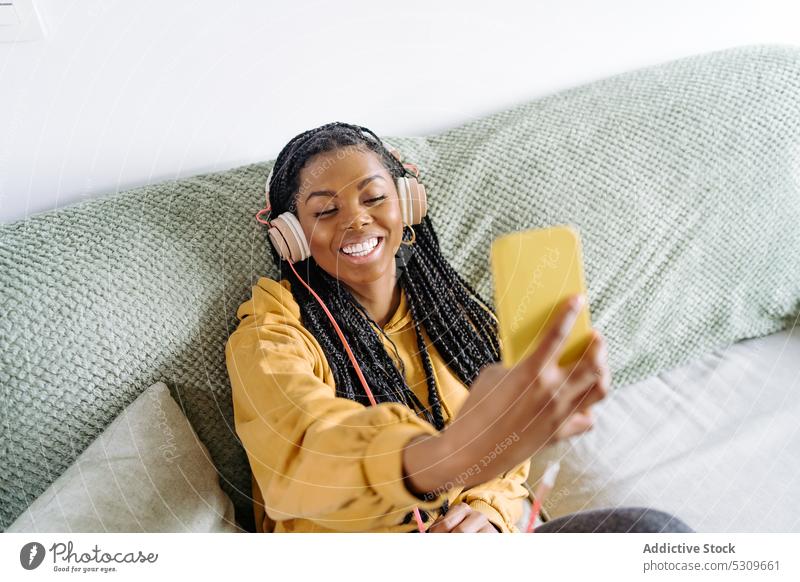 Fröhliche schwarze Frau mit Kopfhörern, die ein Videogespräch auf einem Smartphone führt Videoanruf Lächeln Video-Chat positiv benutzend Kommunizieren heiter