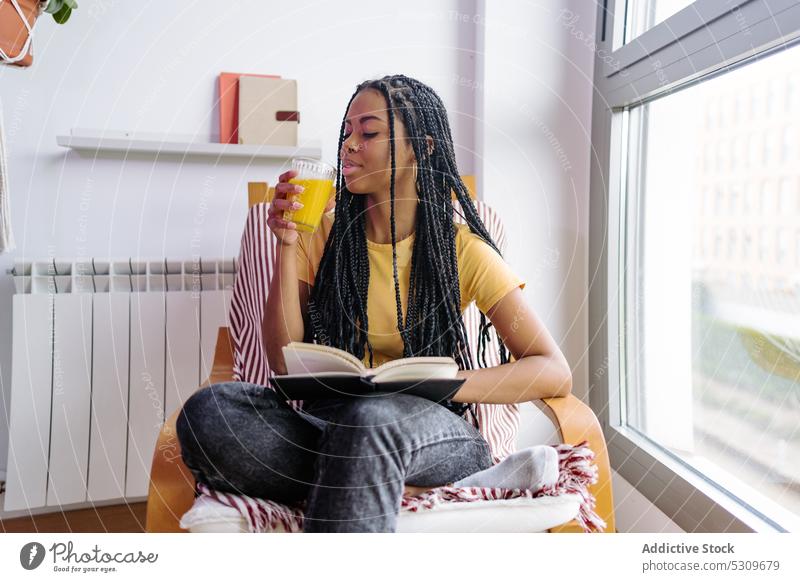 Ruhige schwarze Frau mit Buch trinkt Orangensaft lesen trinken Armsessel Saft ruhen Inhalt heimwärts Literatur jung orange Afroamerikaner ethnisch Getränk