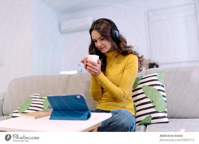 Ruhige Frau mit Tablet, die mit Kopfhörern auf dem Sofa Musik hört zuhören Lächeln Tablette heimwärts benutzend positiv Browsen online Internet jung Glück