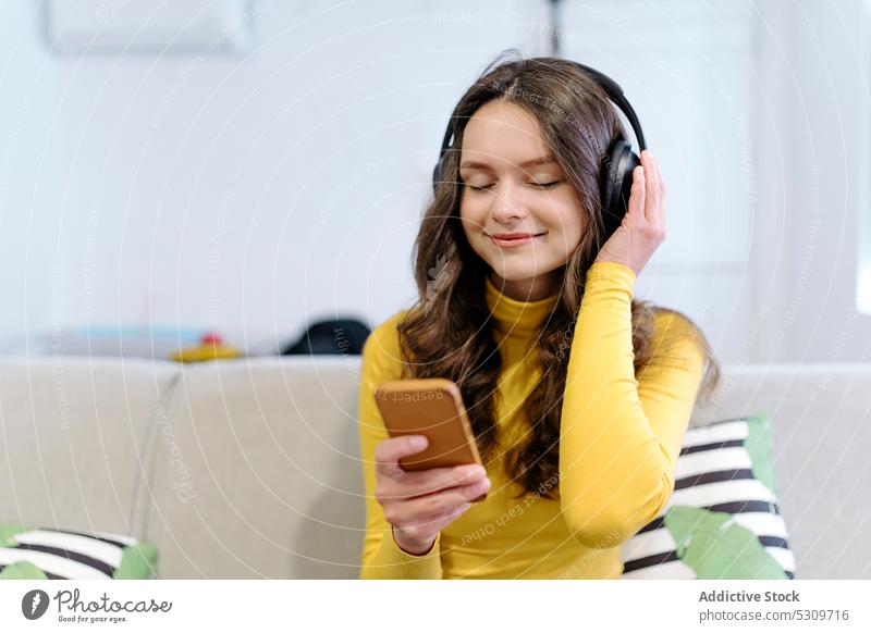 Ruhige Frau mit Smartphone, die mit Kopfhörern auf dem Sofa Musik hört zuhören Lächeln heimwärts Augen geschlossen positiv jung Glück heiter Gerät lässig