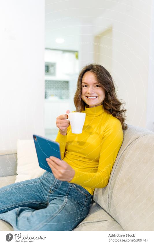 Konzentrierte glückliche Frau mit Kaffee und Tablet auf dem Sofa Tablette benutzend Lächeln Konzentration trinken online heimwärts Freude Wohnzimmer Surfen