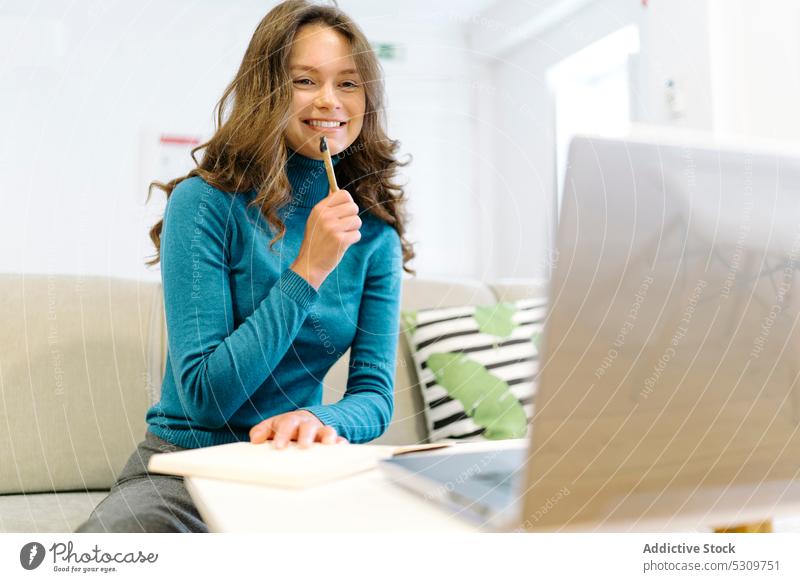 Nachdenkliche Frau mit Stift macht sich Notizen in einem Notizbuch neben einem Laptop auf einer Couch freiberuflich besinnlich zur Kenntnis nehmen Denken