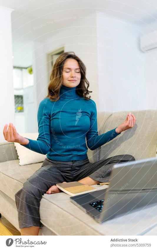 Ruhige Frau meditiert auf dem Sofa während einer Arbeitspause freiberuflich Laptop sich[Akk] entspannen meditieren abgelegen Pause heimwärts jung online