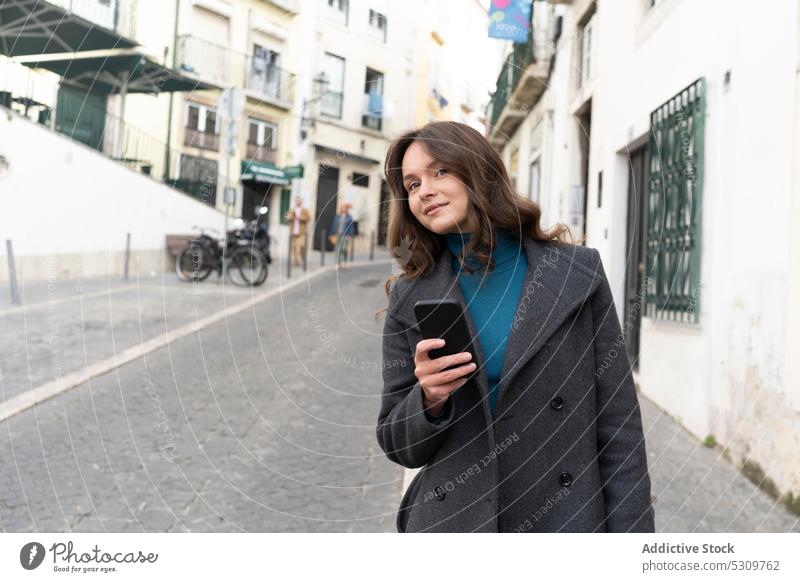 Ruhige Frau, die auf der Straße auf ihrem Smartphone surft und wegschaut Nachricht Großstadt benutzend Talkrunde Internet Stil urban Apparatur Gerät Mantel