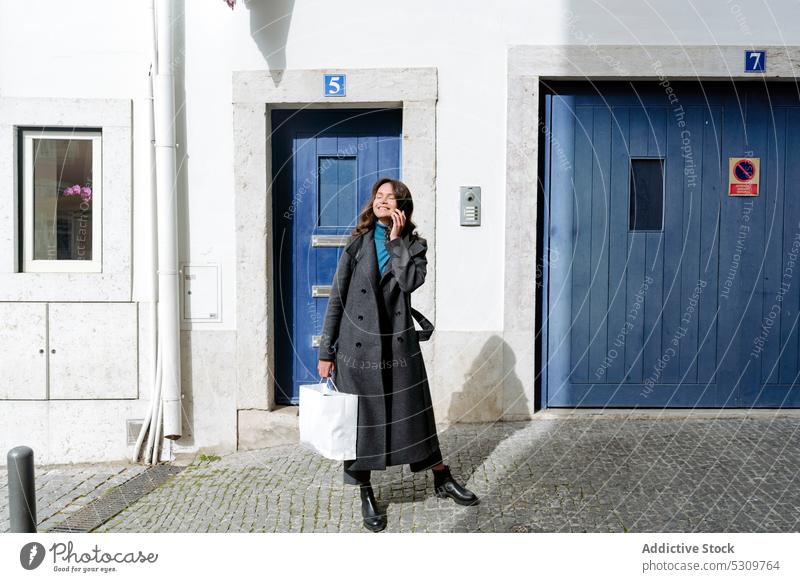 Fröhliche Frau mit Einkaufstasche auf der Straße Eingang Lächeln Glück Straßenbelag Tür Gebäude urban Käufer jung Augen geschlossen heiter Türöffnung Stil