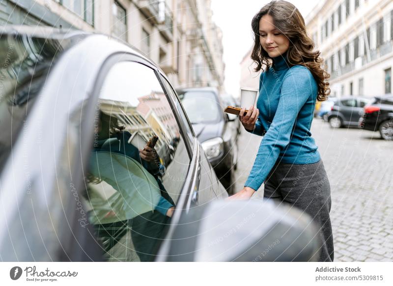 Frau mit Smartphone steht in der Nähe von Auto auf Straße PKW Lächeln positiv Kaffee Großstadt Automobil Fahrzeug Verkehr zum Mitnehmen Imbissbude Einwegartikel