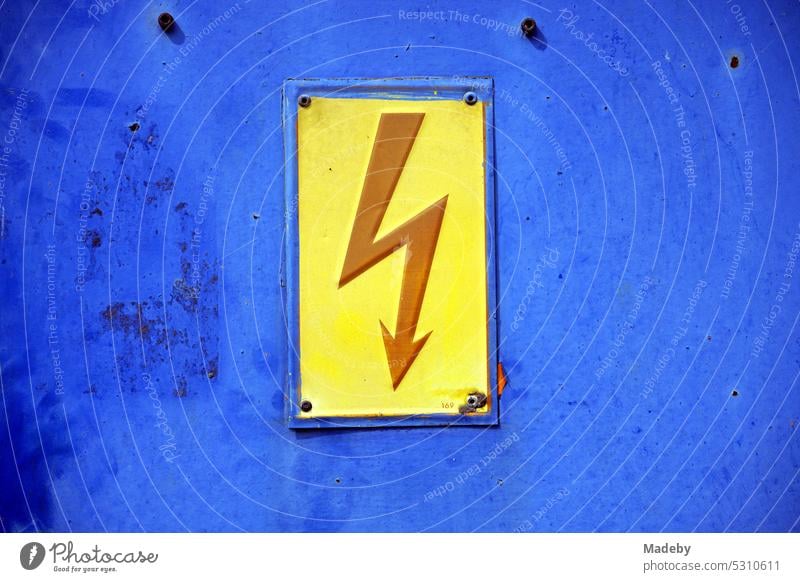 Roter Blitz auf gelbem Grund als Warnung vor Hochspannung auf einem rostigen blauen alten Verteilerkasten am Yachthafen an der Mosel in Traben-Trarbach in Rheinland-Pfalz in Deutschland