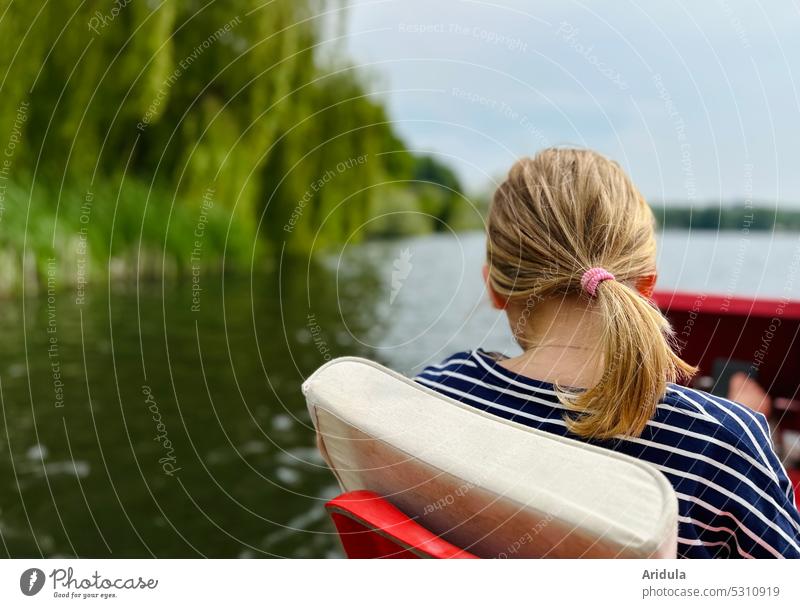 Rückenansicht | Mädchen sitzt im Tretboot auf einem See mit Ufer Kind Wasser Pferdeschwanz Frisur Wasseroberfläche Sonne Schönes Wetter Ausflug Natur