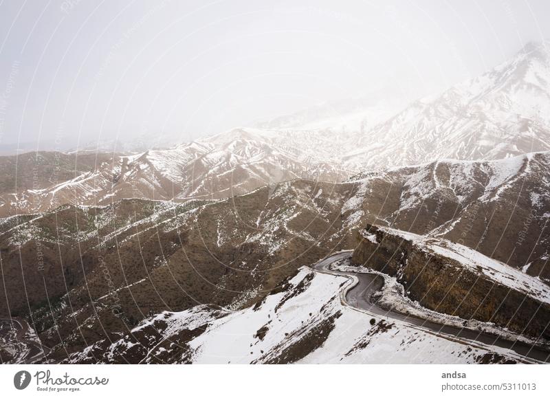 Verschneite, kurvige Straße in den Bergen Hügel Kurve Schnee Braun Pass Nebel mystisch Marokko Atlas Gebirge