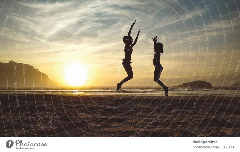 Silhouetten von zwei kleinen Mädchen springen in den Strand bei Sonnenuntergang Kind Freund springend Spielen unkenntlich Sonnenaufgang Sand Fröhlichkeit Glück