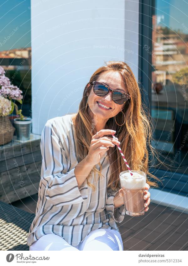 Lächelnde Frau mit Sonnenbrille trinkt einen Milchshake auf einem Dach Porträt Glück elegant Dachterrasse Terrasse trinken attraktiv stylisch Kantine bequem