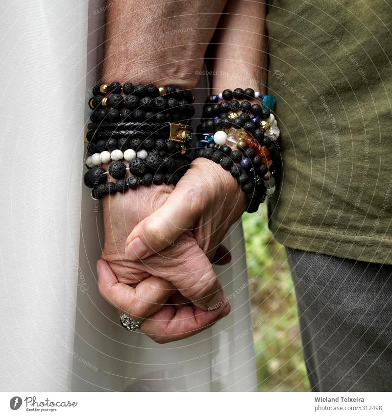 Älterer Mann und Frau halten sich an den Händen. Sie tragen Armbänder aus Lavastein und anderen Materialien. Person Stein weiß natürlich im Freien gealtert