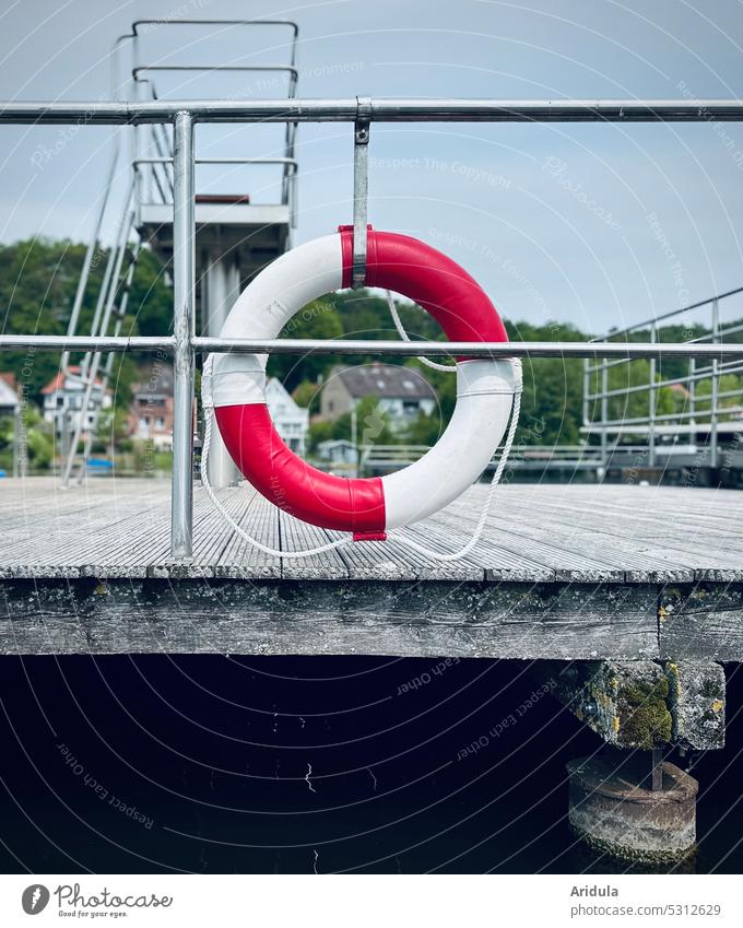 Rettungsring am Geländer eines Stegs am Badesee Boote Springturm Menschenleer Sicherheit Außenaufnahme Buchstaben Gefahr Achtung Vorsicht Risiko Schutz See