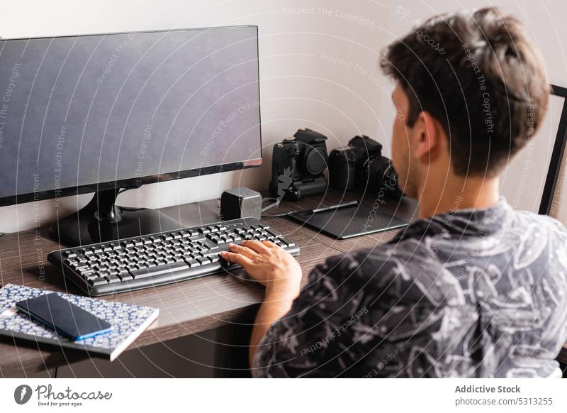 Mann arbeitet am Computer im Heimbüro freiberuflich Arbeitsbereich Arbeitsplatz Telearbeit Smartphone benutzend Gerät Job heimwärts Internet Schreibtisch Stuhl