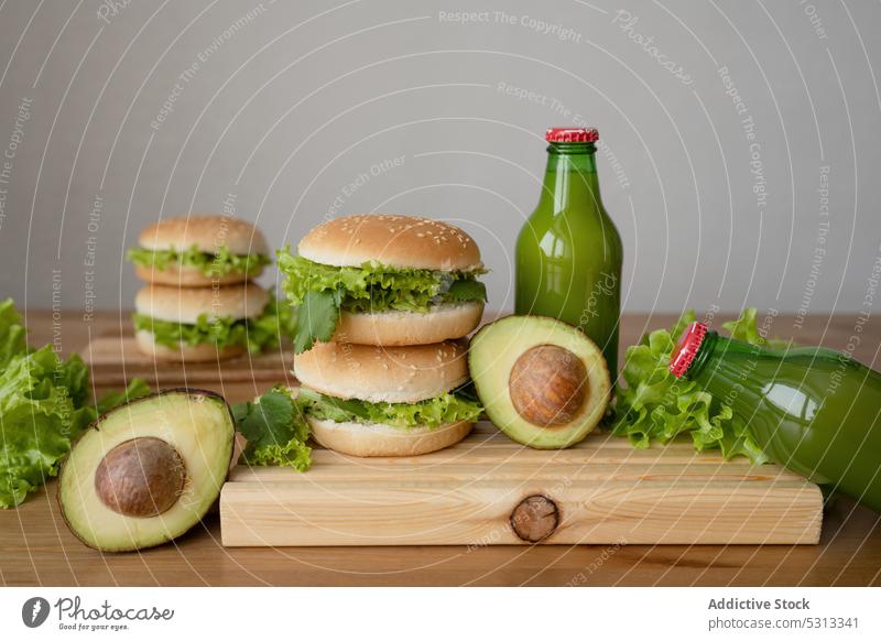 Leckerer Burger mit Gemüse und Avocado auf Holzbrett Hamburger Salat frisch Vegetarier lecker Schneidebrett Flasche Saft Lebensmittel Brötchen Mittagessen