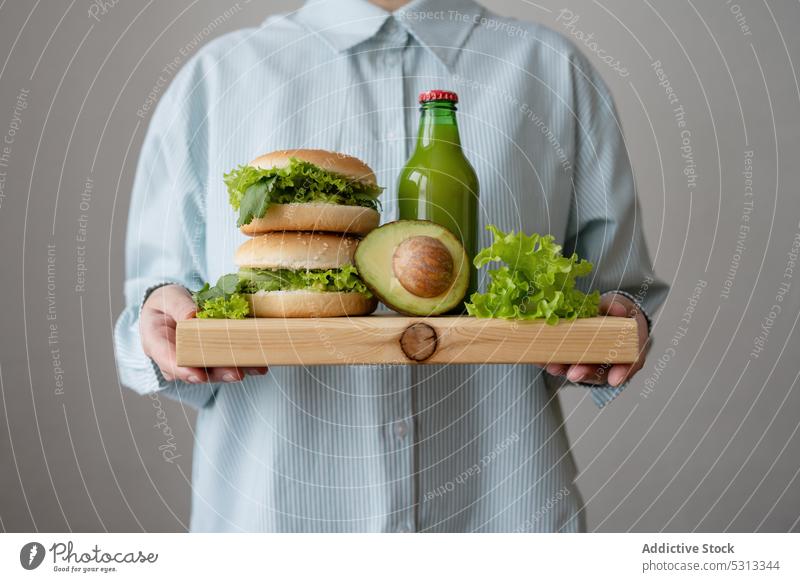 Crop Cook mit veganen Burgern auf Holzschneidebrett Salat Hamburger Vegetarier Avocado hölzern Flasche Saft trinken Erfrischung grün Veganer geschmackvoll