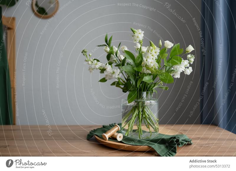 Glasvase mit Blumenstrauß an Bord neben Bändern Vase Bändchen Spule Holzplatte Wasser Blumenladen Werkstatt Floristik eustoma Milchstern Ruscus Lysianthos