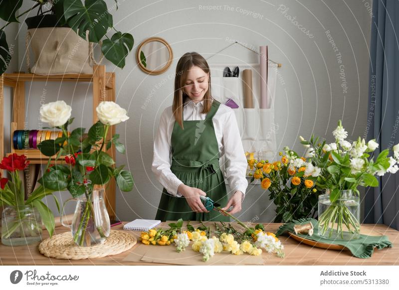 Glückliche Floristin beim Beschneiden von Blumen am Tisch Frau Blumenhändler geschnitten Blumenstrauß Werkstatt positiv Arbeit Lächeln geblümt Job Pflanze