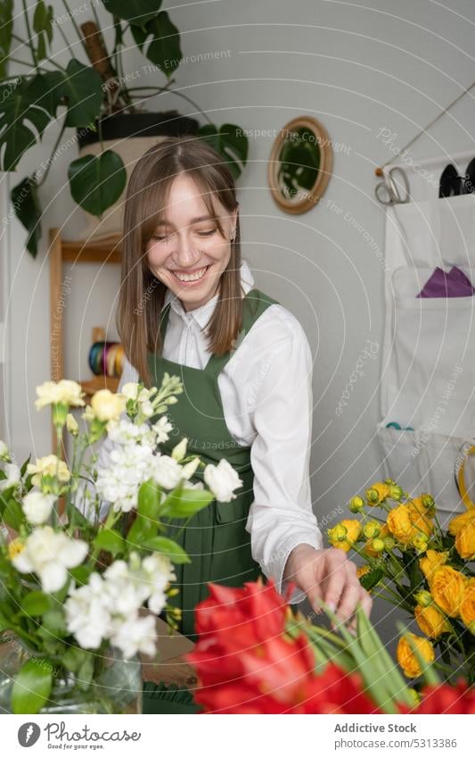 Fröhliche Floristin mit Blumenstrauß Frau Blumenhändler Lächeln Arbeit positiv Werkstatt Floristik Laden Pflanze Schürze Job im Innenbereich Arbeitsplatz