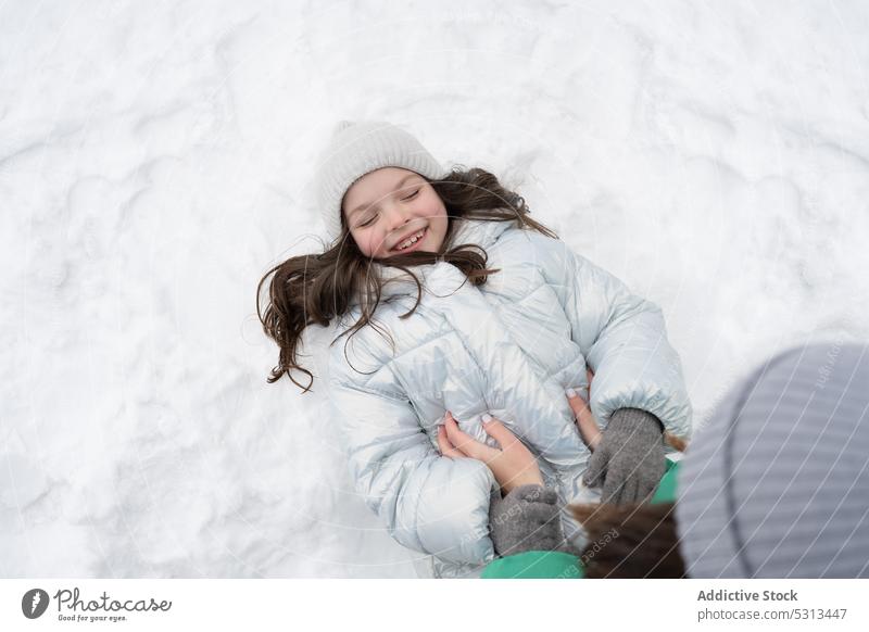 Fröhliches Mädchen in warmer Kleidung auf Schnee liegend Frau Kind Kribbeln Winter Spaß Mutter Liebe Tochter Glück Lächeln heiter Zusammensein Saison Park Natur