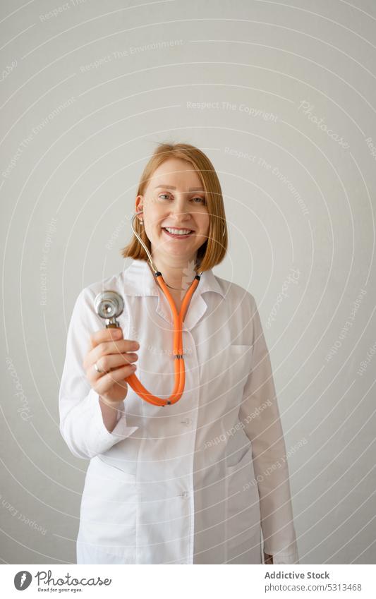 Fröhliche Frau mit Stethoskop im Studio Arzt Uniform zuhören Lächeln professionell Sanitäter Spezialist arzt medizinisch Medizin Klinik Glück Robe jung