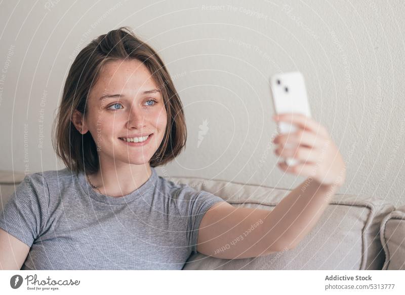 Charmante Frau nimmt Selfie auf Smartphone auf Sofa Freude Kälte heimwärts Selbstportrait Wochenende ruhen benutzend Lächeln Liege Glück Komfort froh Wohnzimmer