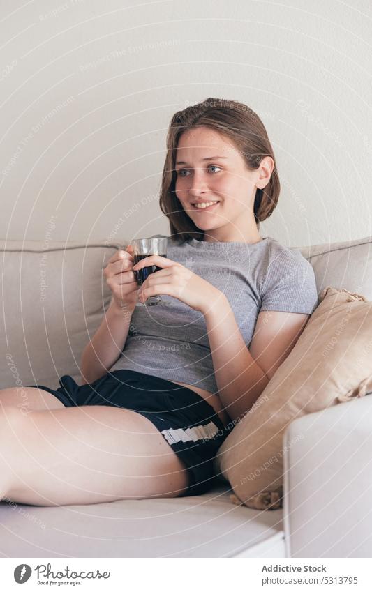 Zufriedene Frau mit einer Tasse Kaffee auf dem Sofa heimwärts trinken positiv Lächeln Frühstück ruhen jung Liege Glück lässig räkeln froh Getränk heimisch