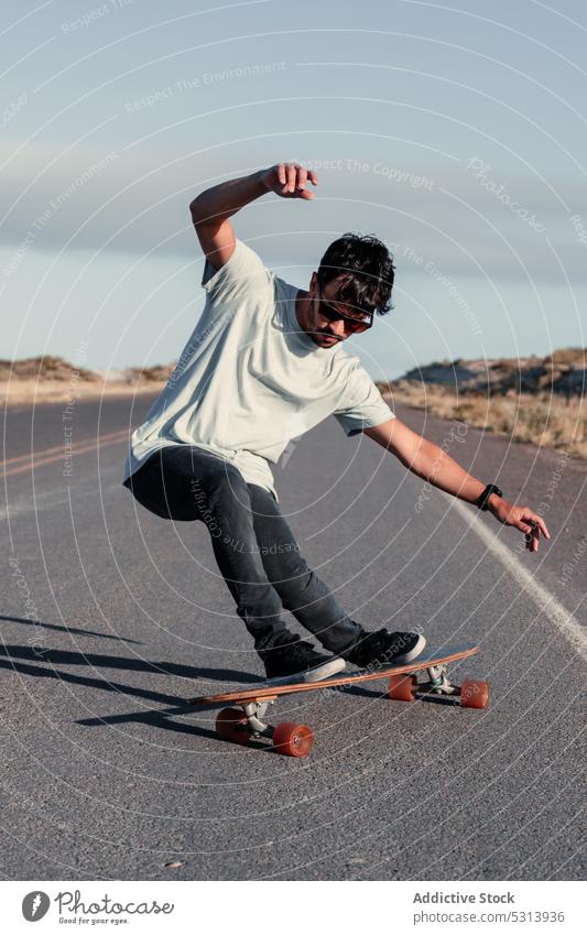 Unbekümmerter Mann balanciert auf einem Skateboard auf einer asphaltierten Straße Trick Skater Mitfahrgelegenheit extrem Adrenalin Gleichgewicht Aktivität