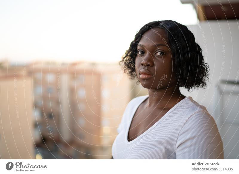 Ruhige schwarze Frau schaut in die Kamera vor einer Stadtlandschaft Vorschein Balkon selbstbewusst Starrer Blick Porträt ernst krause Haare urban Persönlichkeit
