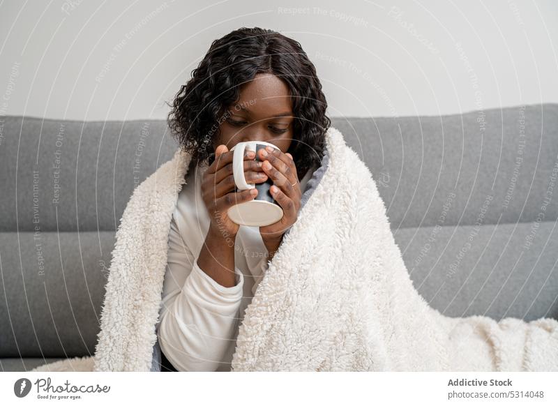 Zufriedene schwarze Frau trinkt heißen Kaffee auf dem Sofa Windstille trinken Heißgetränk Komfort heimwärts gemütlich Getränk Plaid Tasse Liege Afroamerikaner