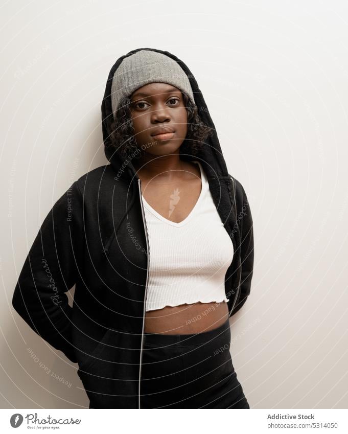 Ruhige schwarze Frau mit Hut schaut in die Kamera ernst selbstbewusst Wand Outfit Stil cool Kapuzenpulli Porträt jung Vorschein Windstille Persönlichkeit