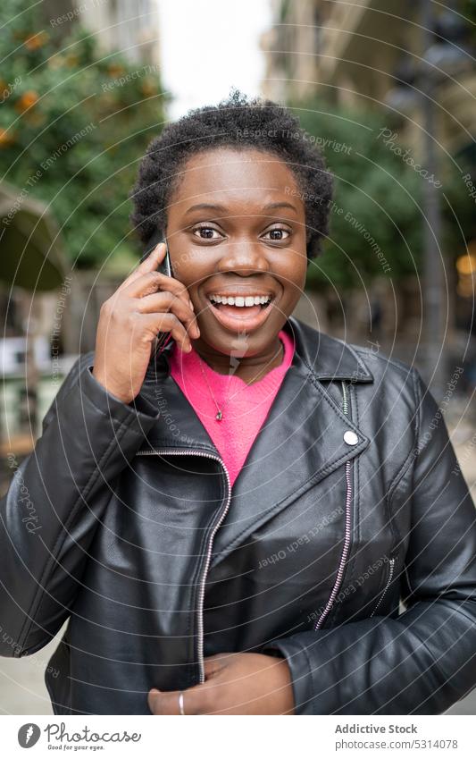 Fröhliche schwarze Frau, die mit einem Smartphone spricht Telefonanruf Straße reden sprechen Gespräch positiv Lächeln jung Afroamerikaner Glück ethnisch heiter