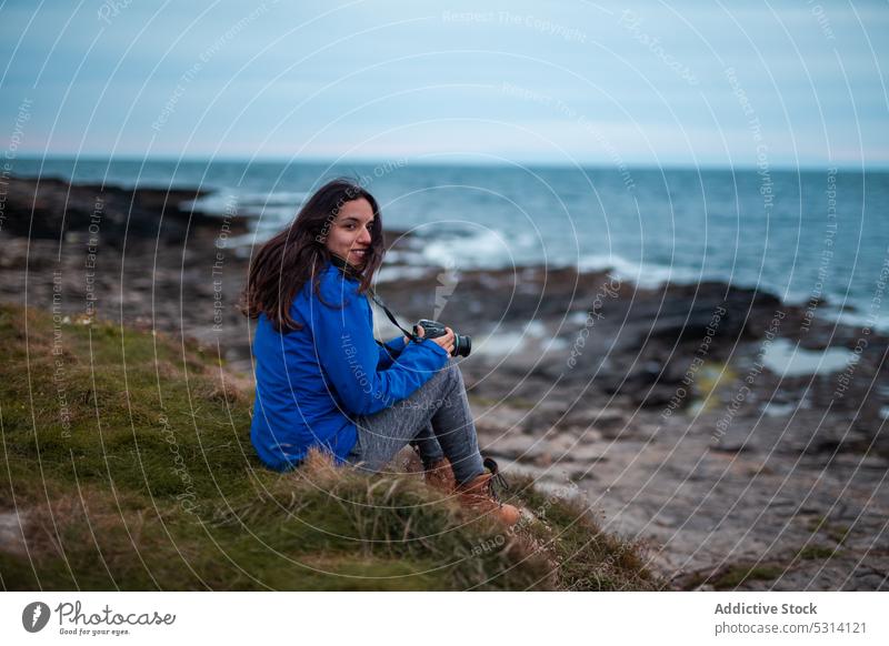 Junge Frau mit professioneller Kamera am Meeresufer sitzend Tourist Fotoapparat Küste Natur Lächeln Urlaub Republik Irland Reisender Fotograf Sonnenuntergang