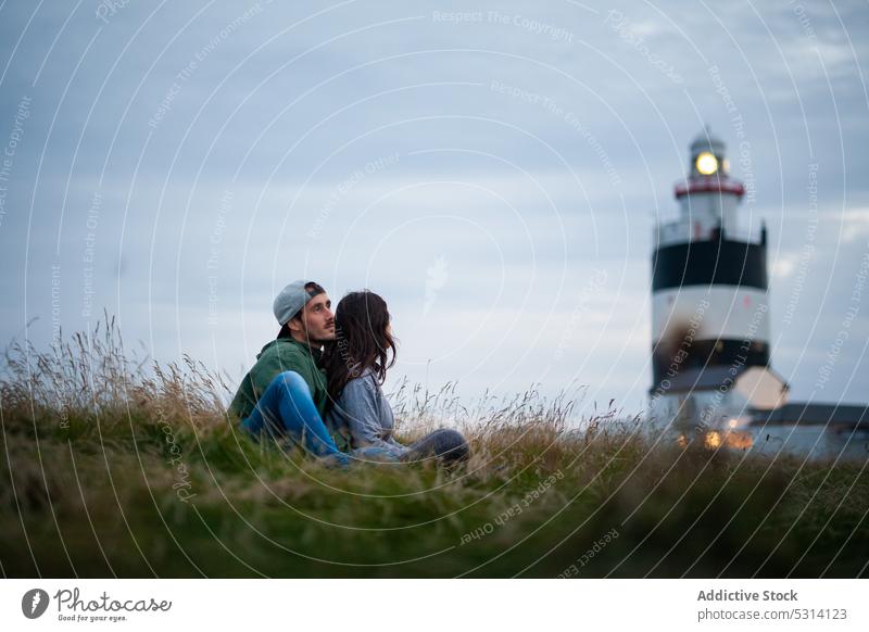 Junges Paar sitzt auf einem Hügel mit Leuchtturm Reisender Landschaft Natur Hochland sich[Akk] entspannen Gras Republik Irland Wochenende Tourist Wiese