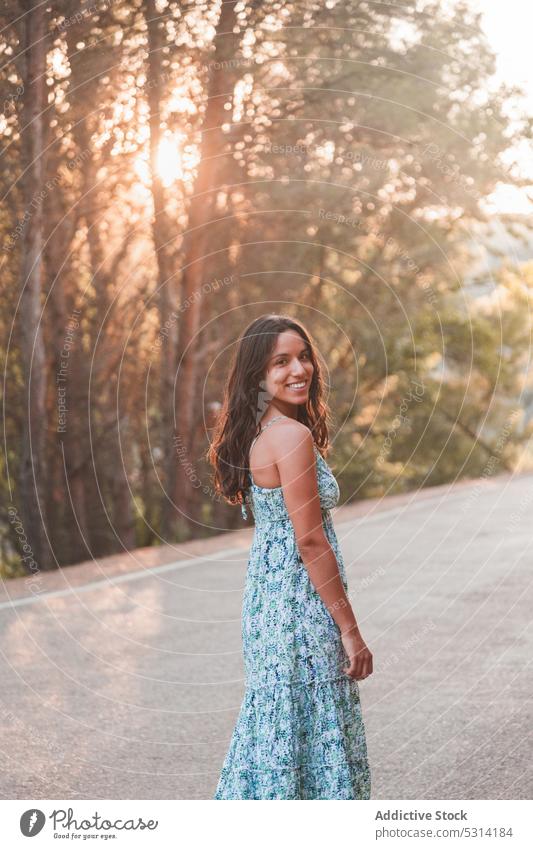 Sorglos lächelnde Frau steht an einer Straße im Wald Reisender Lächeln Asphalt Sommer Sonnenuntergang Glück Großstadt stehen Baum Urlaub Zaragoza bewundern