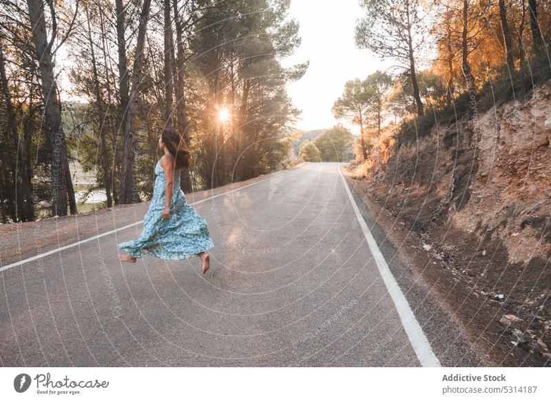 Unbekümmerte Frau springt auf der Straße im Wald Reisender Asphalt Sommer Sonnenuntergang Großstadt springen Baum Urlaub Zaragoza Spanien Kleid Ausflug Abend