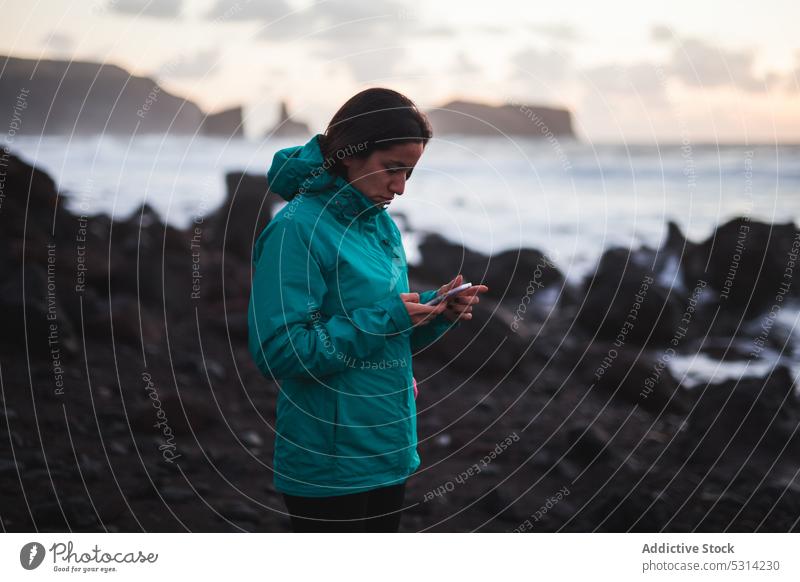 Frau benutzt Smartphone am Meeresstrand benutzend Browsen Reisender Sonnenuntergang Mobile Telefon MEER Ausflug Morgendämmerung warme Kleidung reisen Natur jung