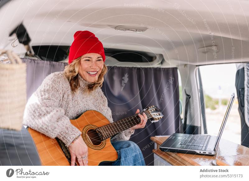 Lächelnde Frau mit Laptop und Gitarre spielen heiter Kleintransporter Musiker Glück Instrument Gerät Freude jung Lifestyle Ausflug Gitarrenspieler ausführen