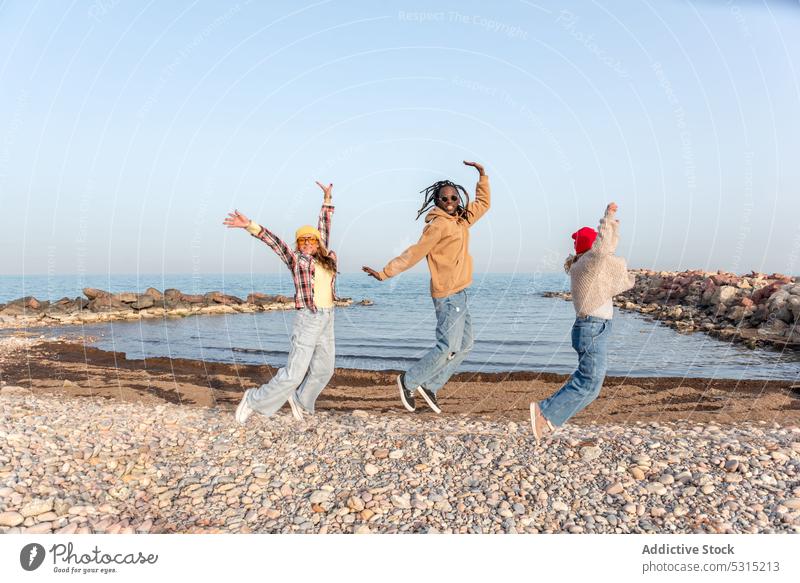 Fröhliche Gruppe verschiedener Freunde, die am Meeresufer springen Frauen Ufer Strand MEER Spaß haben Glück Sommer Freiheit rassenübergreifend vielfältig