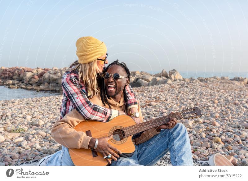 Glückliche diverse Freunde mit Gitarre am Strand Mann Frau spielen Ufer Sommer Lächeln heiter Umarmung Umarmen Musik schwarz ethnisch Afroamerikaner MEER Küste