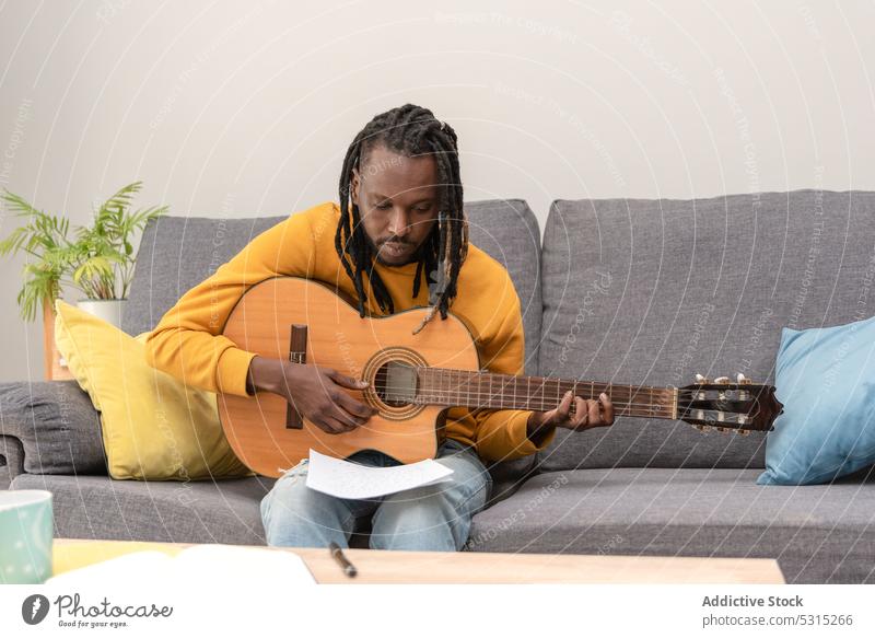 Ernster afroamerikanischer Mann mit Dreadlocks schaut auf ein Papier mit Musiknoten lesen Musiker Rastalocken Gitarre Hobby Instrument Gitarrenspieler