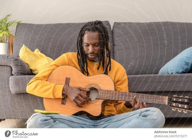 Fröhlicher schwarzer Mann spielt Gitarre Musik Musiker Wohnzimmer Hobby Lächeln spielen heiter Rastalocken Instrument heimwärts Gitarrenspieler Glück männlich