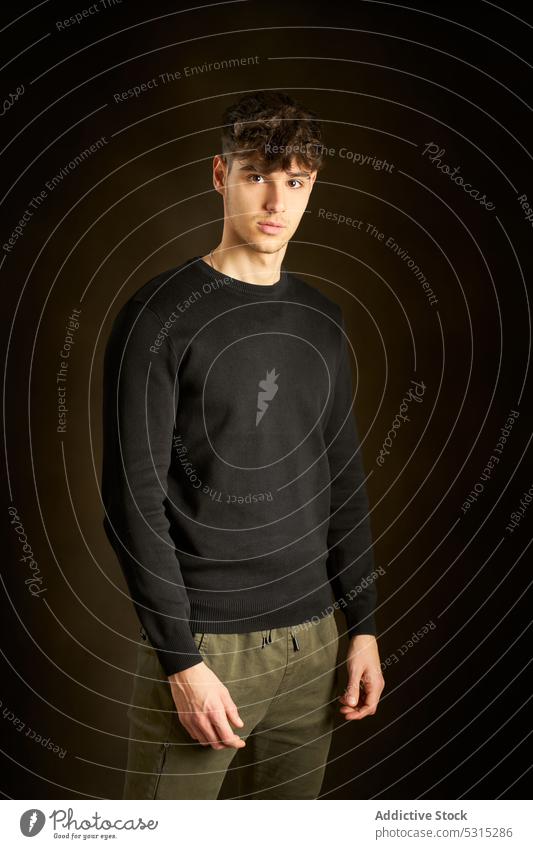 Jugendlicher Junge vor dunkelbraunem Hintergrund Mann Porträt Stil Vorschein Individualität jung freundlich krause Haare Teenager lässig Sweatshirt brünett