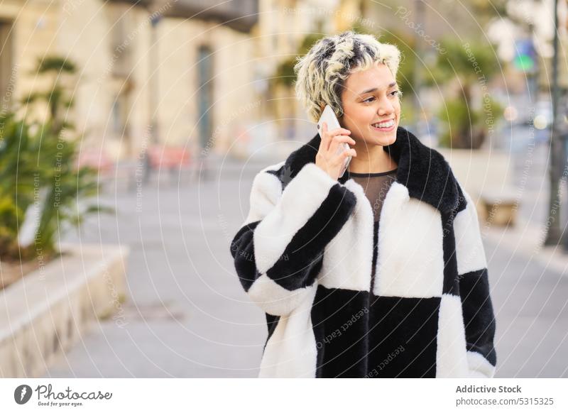 Lächelnde Frau, die auf der Straße mit ihrem Smartphone spricht reden Gespräch Telefonanruf sprechen Stil Glück jung trendy Mantel Gerät heiter Großstadt Mobile