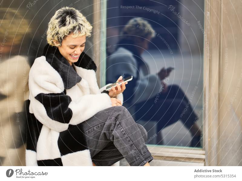 Erfreute Frau mit Smartphone auf der Straße Glück benutzend ruhen Nachricht heiter Gebäude Mantel Großstadt Gerät Browsen Surfen Apparatur Mobile warm Lächeln