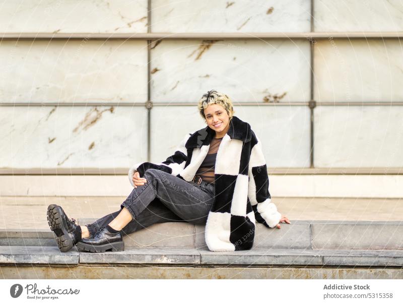 Fröhliche Frau auf der Treppe sitzend Straße Stil Model Vorschein Knie umarmend ruhen Großstadt positiv trendy Outfit Mantel jung Lächeln Stock urban Gebäude