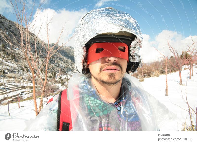eine Person, die eine Superheldenmaske und einen Helm trägt, steht im Schneefeld Wintertag schneebedeckt Held Tracht in die Kamera schauen Outfit Phantasie
