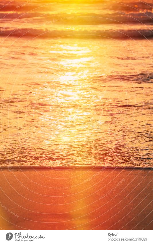 Sonnenuntergang über dem Meer. Riplpe Meer Ozean Wasseroberfläche mit kleinen Wellen. Ozean Wasserschaum splash Waschen Sandstrand. Vertikales Foto aqua