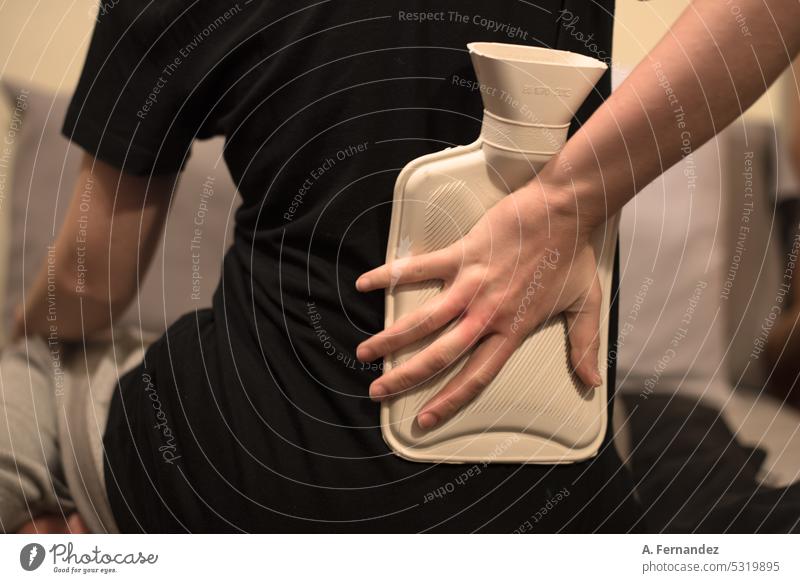 Detail einer Frau, die einen Beutel mit heißem Wasser auf den unteren Rückenbereich legt, um Schmerzen durch Wärmetherapie zu lindern Bettwärmer Heizkörper